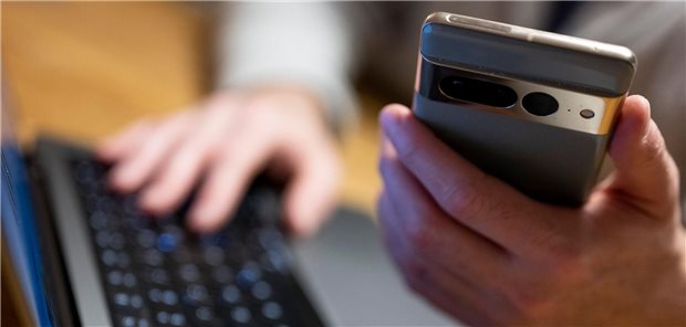Große Mehrheit der Deutschen offen für KI in Gesundheitsversorgung Ein Mann sitzt am Laptop und hält ein Smartphone mit in der Hand.