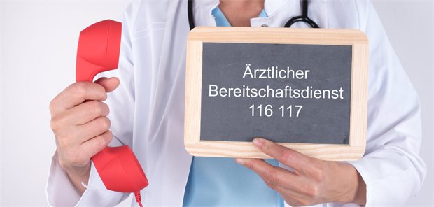KV Saarland wehrt sich mit BDP-Schließung gegen Zusatz-Belastungen Arzt hält rotes Telefon in der Hand und in der andren ein Schild mit der Aufschrift „Ärztlicher Bereitschaftsdienst 116 117“.