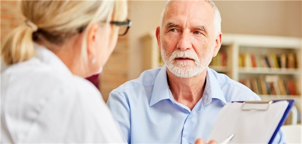 Ärztin spricht mit einem älteren Patienten und macht sich Notizen.