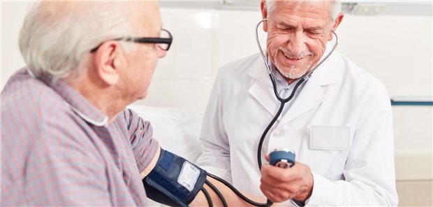 Arzt misst Blutdruck eines älteren Herren und lächelt