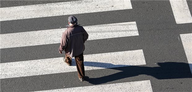 Gehtraining bei pAVK: Wie Hausärzte unterstützen können Ein älterer Mann geht über einen Zebrastreifen.
