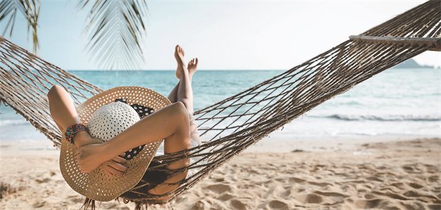 Reisedermatosen: Wie vorgehen bei den drei häufigsten Tropenparasiten? Eine Frau liegt entspannt vor dem Meer in einer Hängematte.