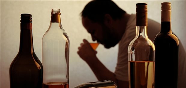 Wie lebenslanger Alkoholkonsum das Darmkrebsrisiko steigert Ein Mann im Hintergrund nimmt einen Schluck von einem Drink. Im Vordergrund stehen vier Flaschen mit alkoholischen Getränken.