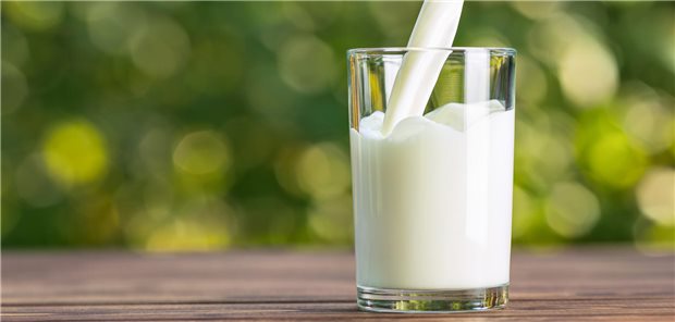 Milch wird aus einer Flasche in ein Glas auf einem Holztisch im Freien gegossen.