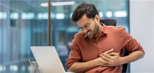 Geschäftsmann verspürt Schmerzen in der Brust während der Arbeit am Schreibtisch in einem modernen Büro.