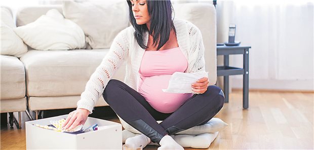 Eine schwangere Frau sitzt auf dem Fussboden ihres Wohnzimmers und liest die Packungsbeilage eines Medikaments. &#xA;&#xA;Usage: Online (20210812)