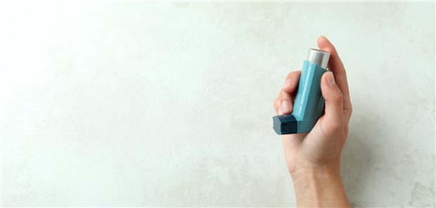 Eine Hand hält einen Asthma-Inhalator in die Höhe-