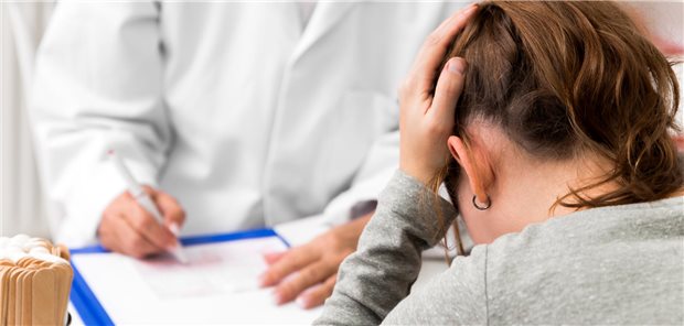 Patienten mit unklaren Beschwerden? Wann es eine somatische Belastungsstörung ist Eine Patientin schlägt die Hände auf dem Kopf zusammen. Gegenüber sitzt ein Arzt in weißem Mantel.
