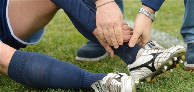 Das ist bei Sprunggelenksverletzungen zu beachten Ein Fußballspieler hält sich seinen Knöchel, ein Helfer assistiert ihm.