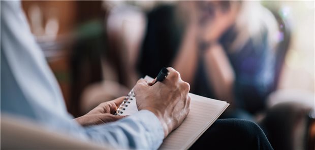 Depressionen: Ein Kernthema auch für Hausärzte! Ein Psychoterapeut spricht mit einer Patientin un dhält einen Block und Stift in der Hand.
