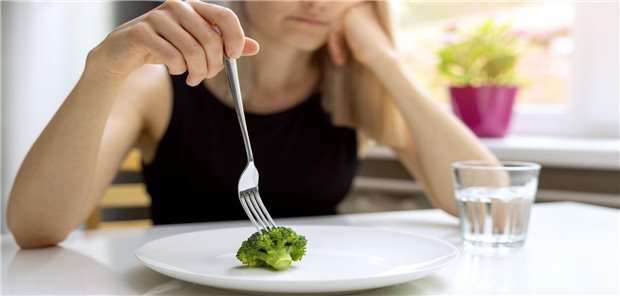 Junge Frau stochert auf kleinem Broccoli auf leerem Teller herum