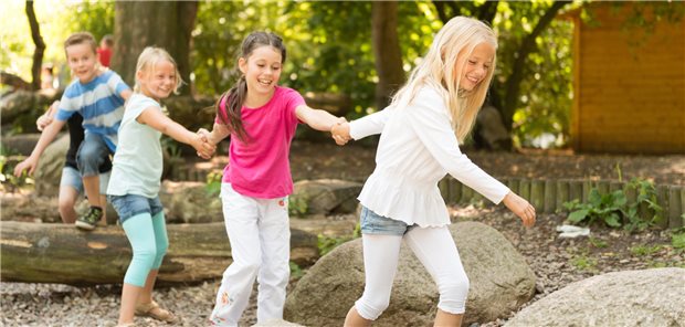 BVKJ-Medienpreis 2026: „Wir wollen bewusst Positivbeispiele zeigen“ Kinder im Grundschulalter, die sich an den Händen halten und auf einem Spielplatz über Baumstämme klettern
