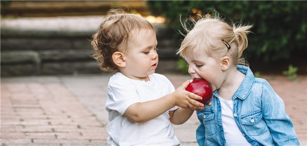 Zwei Kinder teilen sich einen Apfel.