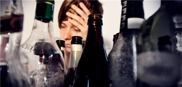 Suchterkrankungen: Stigmatisierung durch medizinisches Personal erschwert Therapie Eine Frau sitzt hinter vielen leeren Flaschen