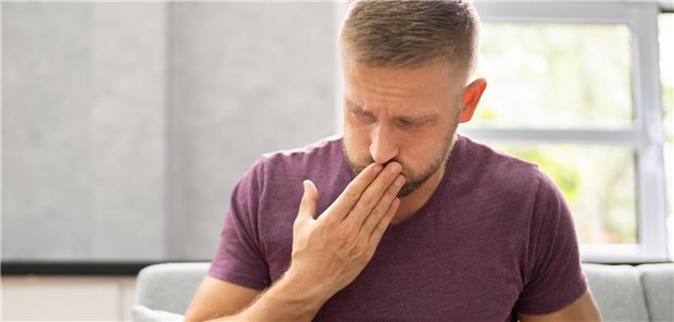 Häufiges Aufstoßen: Woher es kommen kann und wie therapiert wird Ein Mann muss aufstoßen und hält sich die Hand vor den Mund.