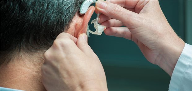 Hörgeräteversorgung bei Demenz: Risikominderung je nach Altersgruppe Ein Arzt setzt ein Hörgerät in das rechte Ohr eines Mannes ein.
