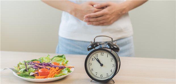 Intermittierendes Fasten könnte Beschwerden bei Adipositas und Morbus Crohn lindern Eine Uhr und ein Salat stehen auf dem Tisch.