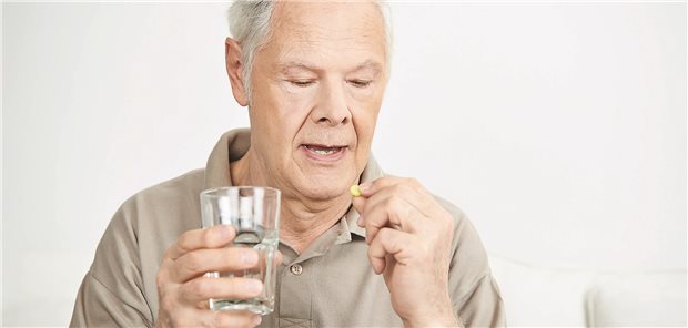 Ein älterer Mann nimmt eine kleine Tablette ein und hält ein Wasserglas in der Hand.