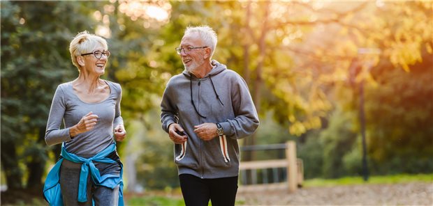 Wie körperliche Aktivität das Wohlbefinden im Alltag verbessert Eine ältere Frau und ein älterer Mann joggen im Park bei Sonnenuntergang.