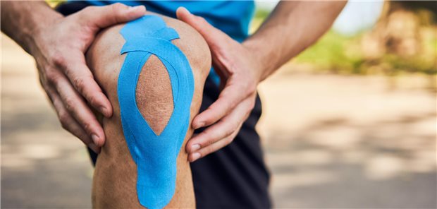 Was bringt Kinesiotaping? Ein Läufer, der sein Knie mit blauem Tape versorgt hat.