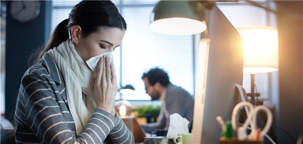 Krank zur Arbeit – das erhöht das Fatigue-Risiko Eine Frau sitzt vor dem PC und schneuzt in ein Taschentuch.