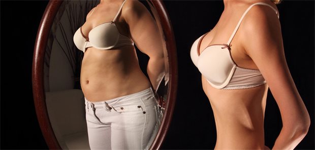 Weltweit immer mehr Fälle von Anorexie und Bulimie Eine schlanke Frau sieht sich selbst im Spiegel und sieht einen dicken Bauch.