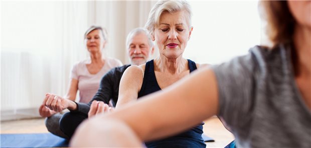 Yoga lindert Fatigue und bessert die Stimmung bei Krebsüberlebenden Vier ältere Personen sitzen in einem Raum im Schneidersitz und machen eine Yoga-Übung.