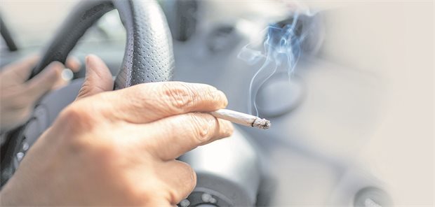 Wie viele KHK-Patienten rauchen? Eine Frau sitzt mit einer brennenden Zigarette hinter dem Lenkrad ihres Autos.