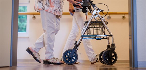 Arbeitgeberverband ruft Linnemann zu Kurswechsel in der Pflegepolitik auf Eine Pflegekraft geht in einem Pflegeheim mit einer älteren Frau über einen Korridor. Die Frau schiebt einen Rollator.