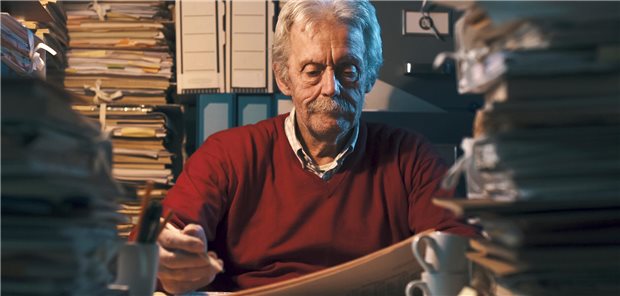 Regressbescheid nach 10 Jahren – ist das rechtens? Älterer Mann sitzt in einem dunklen Raum umgeben von einem Stapel Akten.