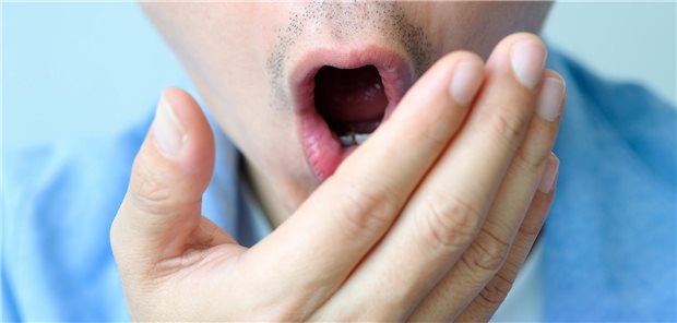 Ursache für Mundgeruch finden: 3 Tests für die Halitosis-Untersuchung Ein Mann hält sich die Hand vor den Mund, um seinen eigenen Mundgeruch zu riechen.