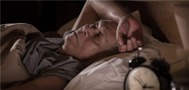 Parkinson: Wieso guter Schlaf besonders präventiv wirkt Ein älterer Mann liegt wach im Bett und kann nicht schlafen. Eine Uhr auf dem Nachtkasten zeigt kurz vor 3 Uhr an.