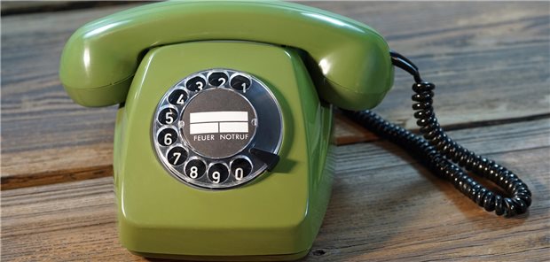 KBV zu geplanten strengeren Vorgaben bei Krankschreibung: „Das ist Misstrauen!“ Ein grünes Telefon mit Wählscheibe steht auf einem Holztisch.