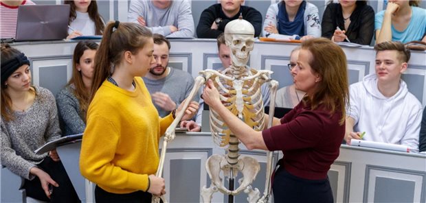 Masterplan ade: Fakultäten schreiben Medizinstudium in eigener Regie fort Medizinstudierende schauen einer Dozentin beim Erklären eines menschlichen Skeletts zu.