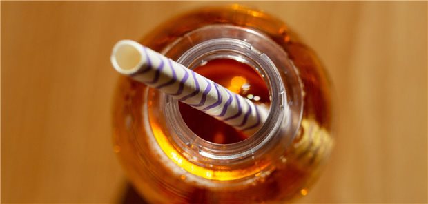 Warum sich 4.000 Ärztinnen und Ärzte für die Zuckersteuer aussprechen Eine geöffnete Flasche mit einem zuckerhaltigen Erfrischungsgetränk steht auf einem Tisch, in der Öffnung steckt ein Trinkhalm.