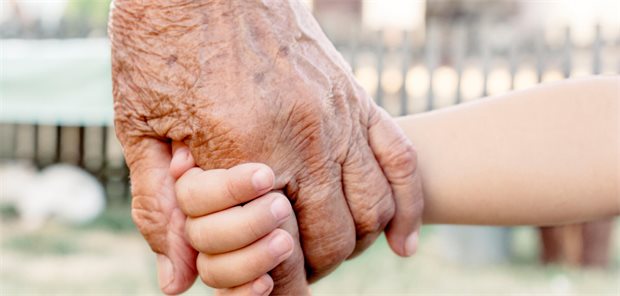 Kinderlosen-Zuschlag in der Pflegeversicherung: Generationengerecht oder Strafzahlung? Das Foto zeigt die Hand eines alten Menschen und eines Kindes, die ineinandergreifen.