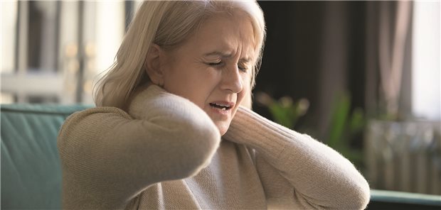 Frau fasst sich in den Nacken und verzerrt vor Schmerzen das Gesicht