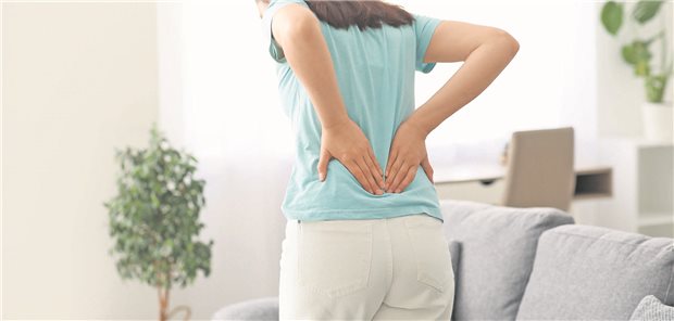 Akute Rückenschmerzen: Was bringt die spinale Manipulation? Eine junge Frau hält sich bei Rückenschmerzen beide Hände an den unteren Rücken.