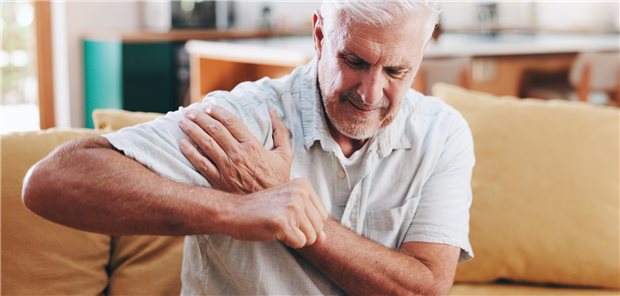 Schulterschmerzen: Subakromiale Dekompression ohne langfristigen Nutzen bei Impingement Ein Mann sitzt auf einem Sofa und legt die linke Hand auf die rechte Schulter, die schmerzt.