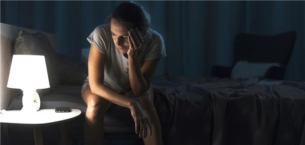 Stufenschema bei Insomnie: So bei Schlafstörungen therapieren Frau sitzt nachts auf ihrem Bett und schaut ins Licht ihrer Nachttischlampe.