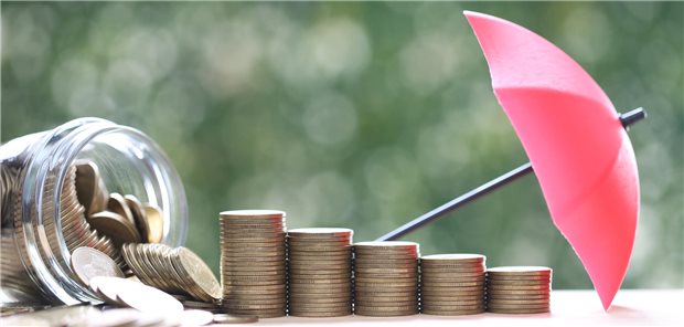 Grundlage für erfolgreiche Geldanlage: Das eigene Risikoprofil verstehen Geldmünzen zu Säulen gestapelt, davor ein Mini-Regenschirm, um Schutz vor Risiken zu symbolisieren.