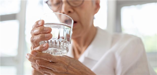 Woher kommen die Armzuckungen im Herzrhythmus einer Patientin? ältere asiatische Frau trinkt aus einem Wasserglas und stützt sich den Arm dabei