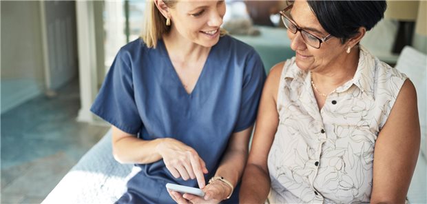 DiGA, Neugeborenen-Screening, Heilmittelzuzahlung und Trisomietest: Das ändert sich ab April Eine junge MFA zeigt einer älteren Frau eine Anwendung auf einem Smartphone.